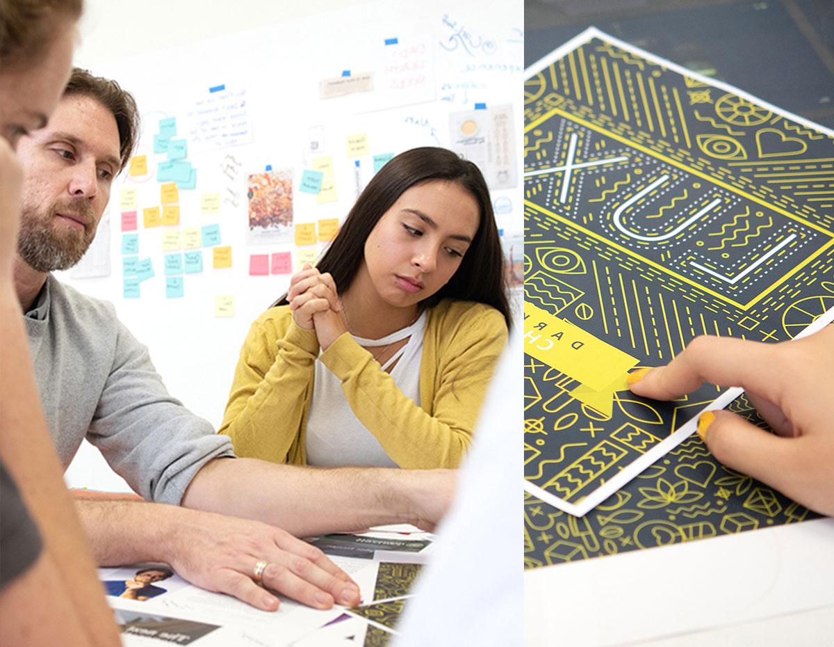 Students sitting at a table reviewing a poster design with instruction and guidance by a design professor.